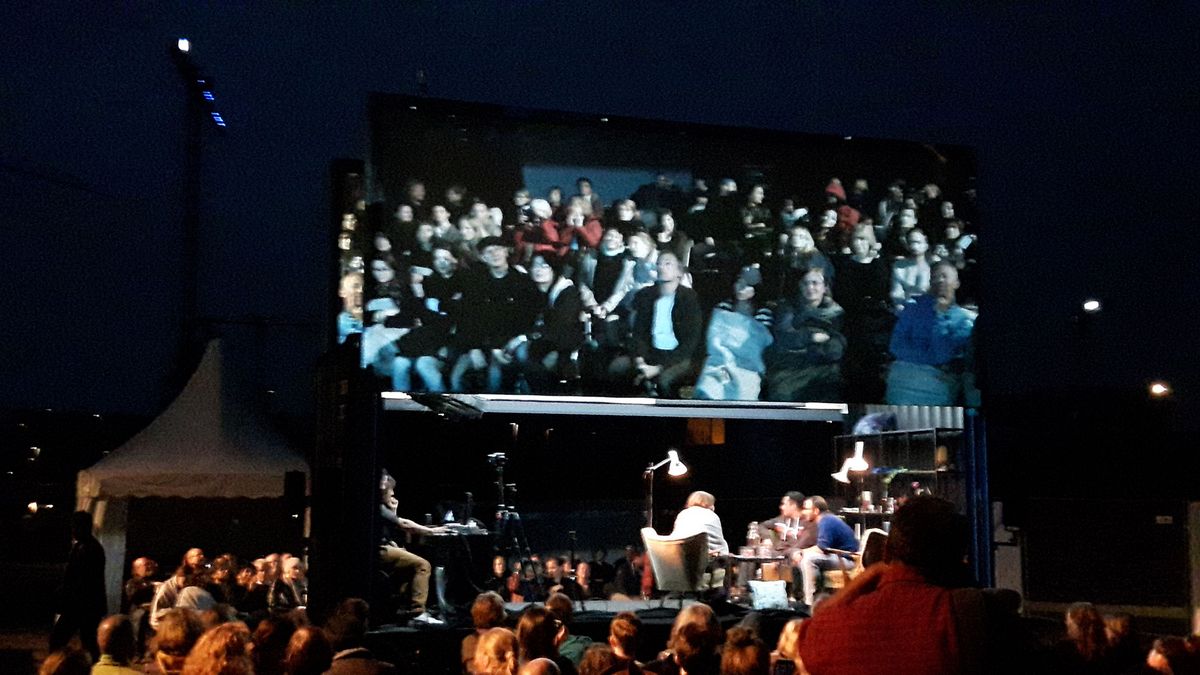 zur Vergrößerungsansicht des Bildes: Bühne bei einer Abendveranstaltung von "Theater der Welt"; auf einer Leinwand darüber ist das Publikum zu sehen